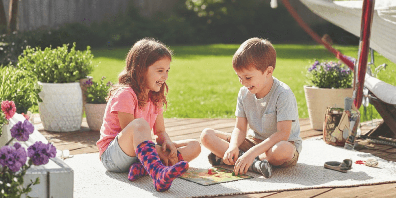 The image features two children joyfully playing a board game outdoors, symbolizing the warmth, comfort, and inclusivity of Polar Feet products.