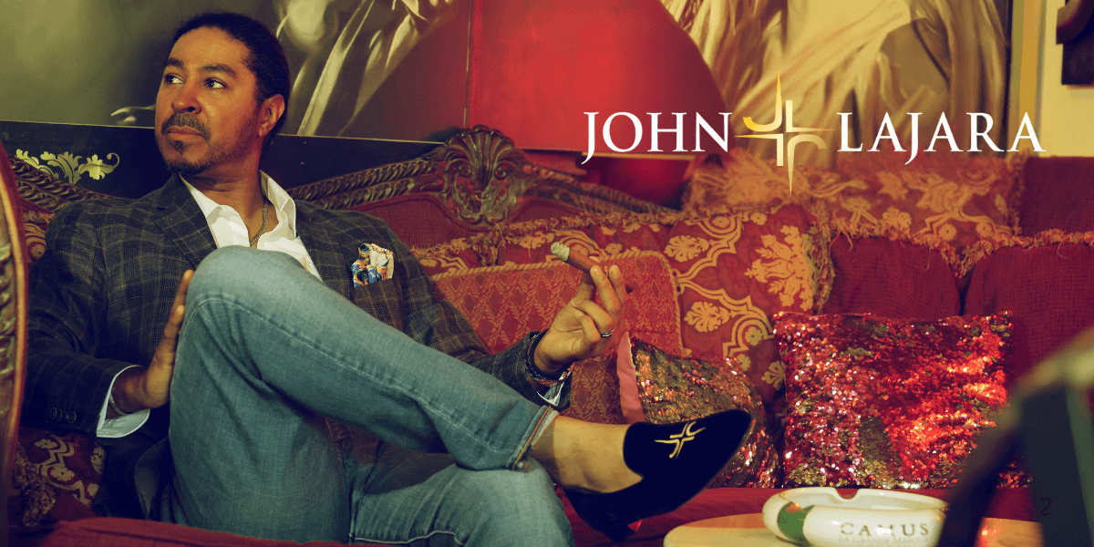John Lajara lounges confidently in a luxurious setting, showcasing his exclusive footwear brand with elegance and style.