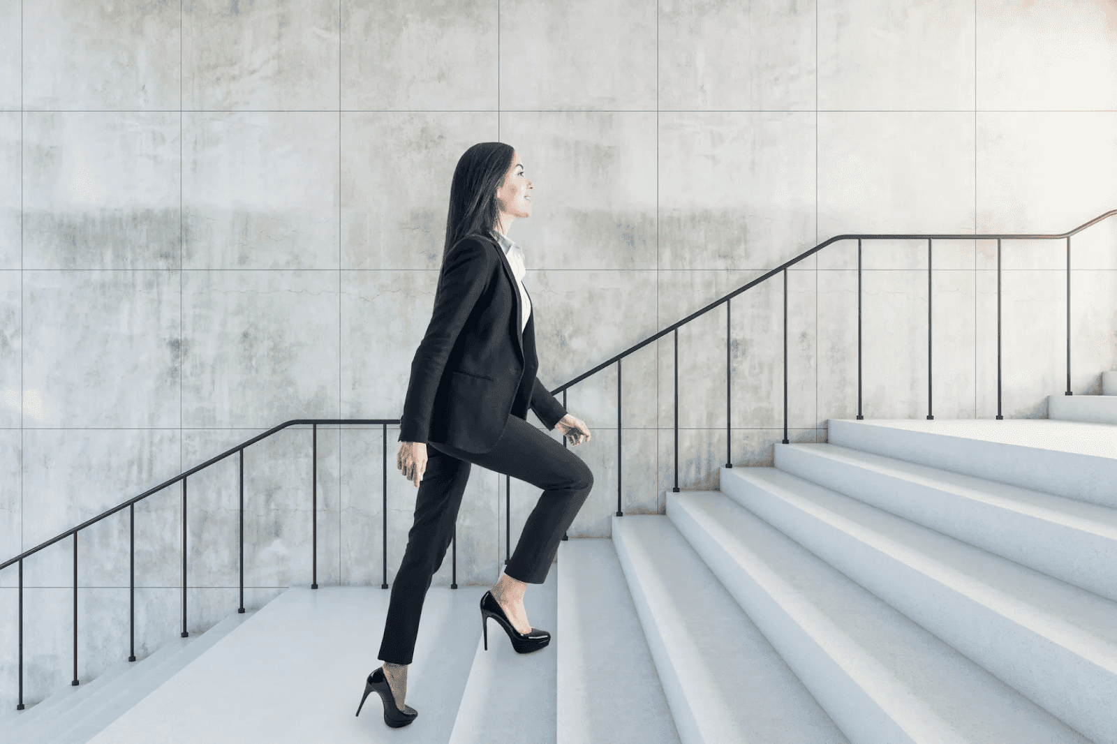Woman in business suit confidently walking up modern white staircase.