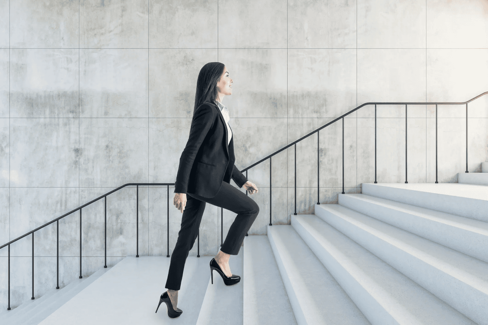 Woman in business suit confidently walking up modern white staircase.