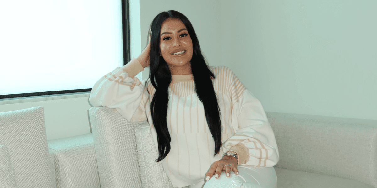 Erica Battista seated on a light-colored sofa, smiling in a neutral indoor setting.