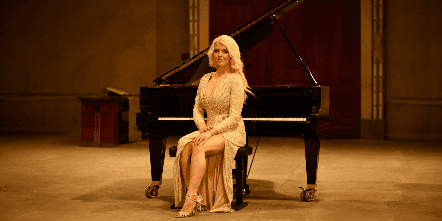 Ellen Fischerová in a sparkling gold gown seated at a black grand piano onstage.