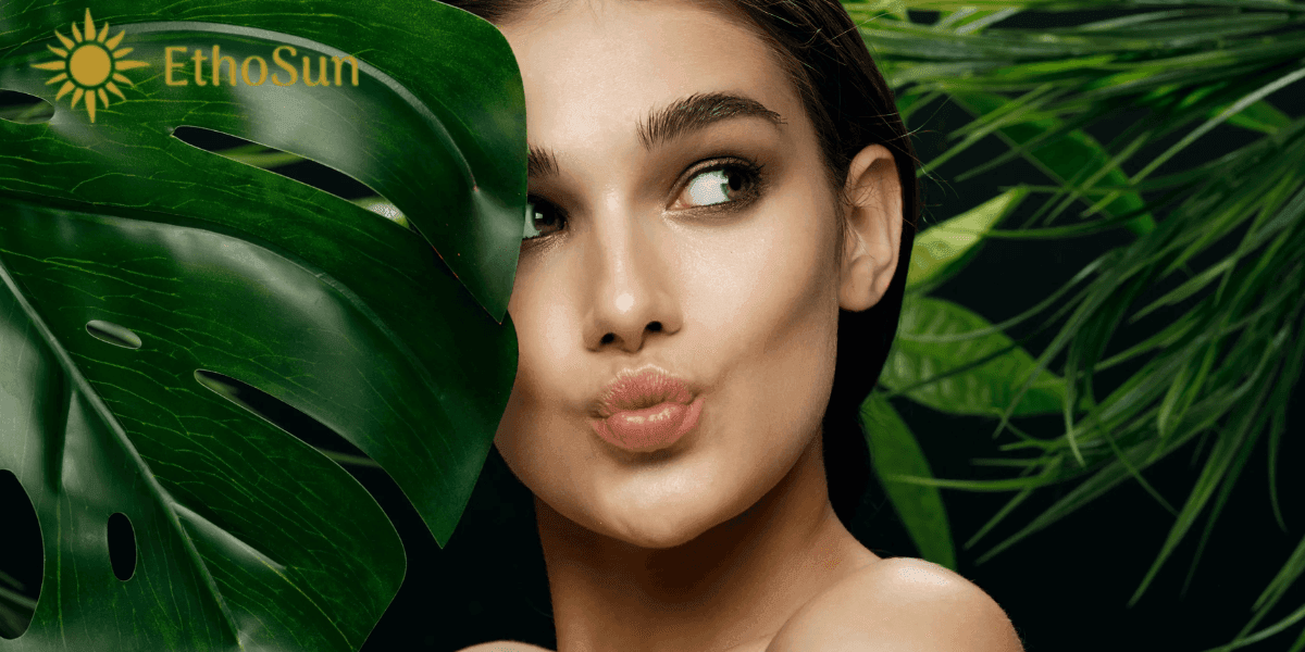 Woman with glowing skin behind tropical leaves, showcasing EthoSun’s natural, sustainable, and eco-friendly sun care products.