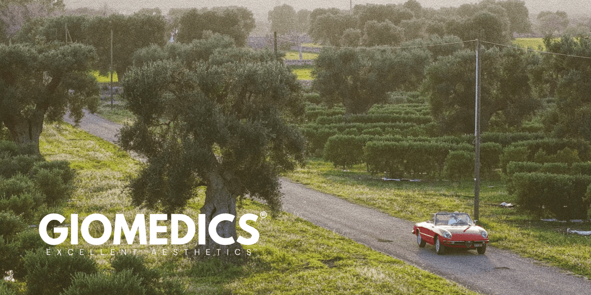 Red convertible driving through olive groves, reflecting GIOMEDICS® European lifestyle and brand identity.