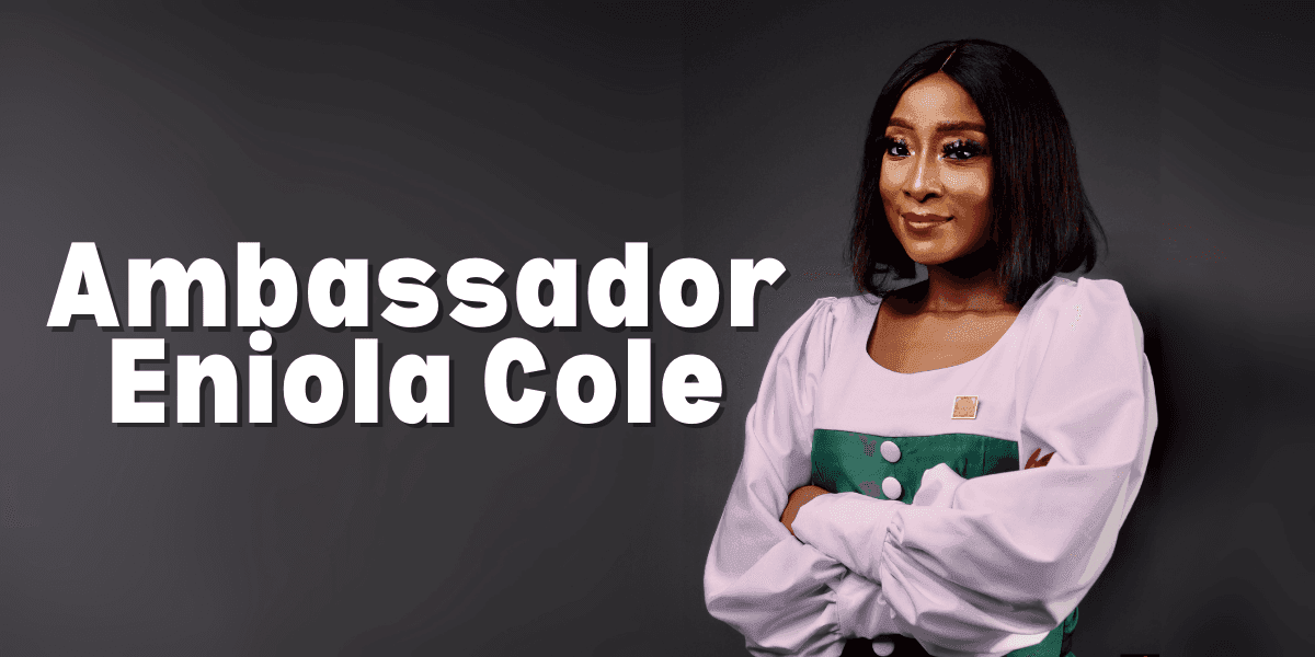 "Portrait of Ambassador Eniola Cole, wearing a white and green dress, posing confidently with her arms crossed in front of a neutral background."