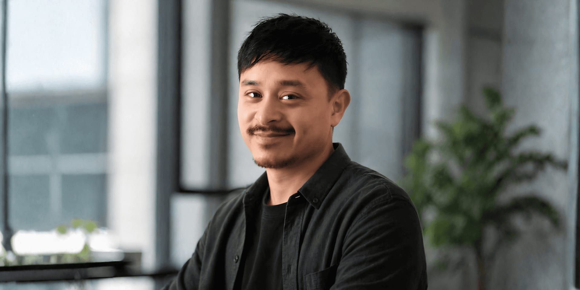 Man with short dark hair and mustache smiling in a modern office setting.