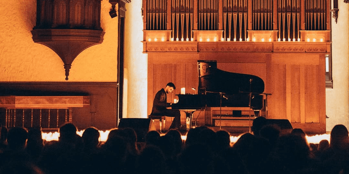 "Pianist performing live in a grand hall with illuminated organ pipes, candles, and an engaged audience."
