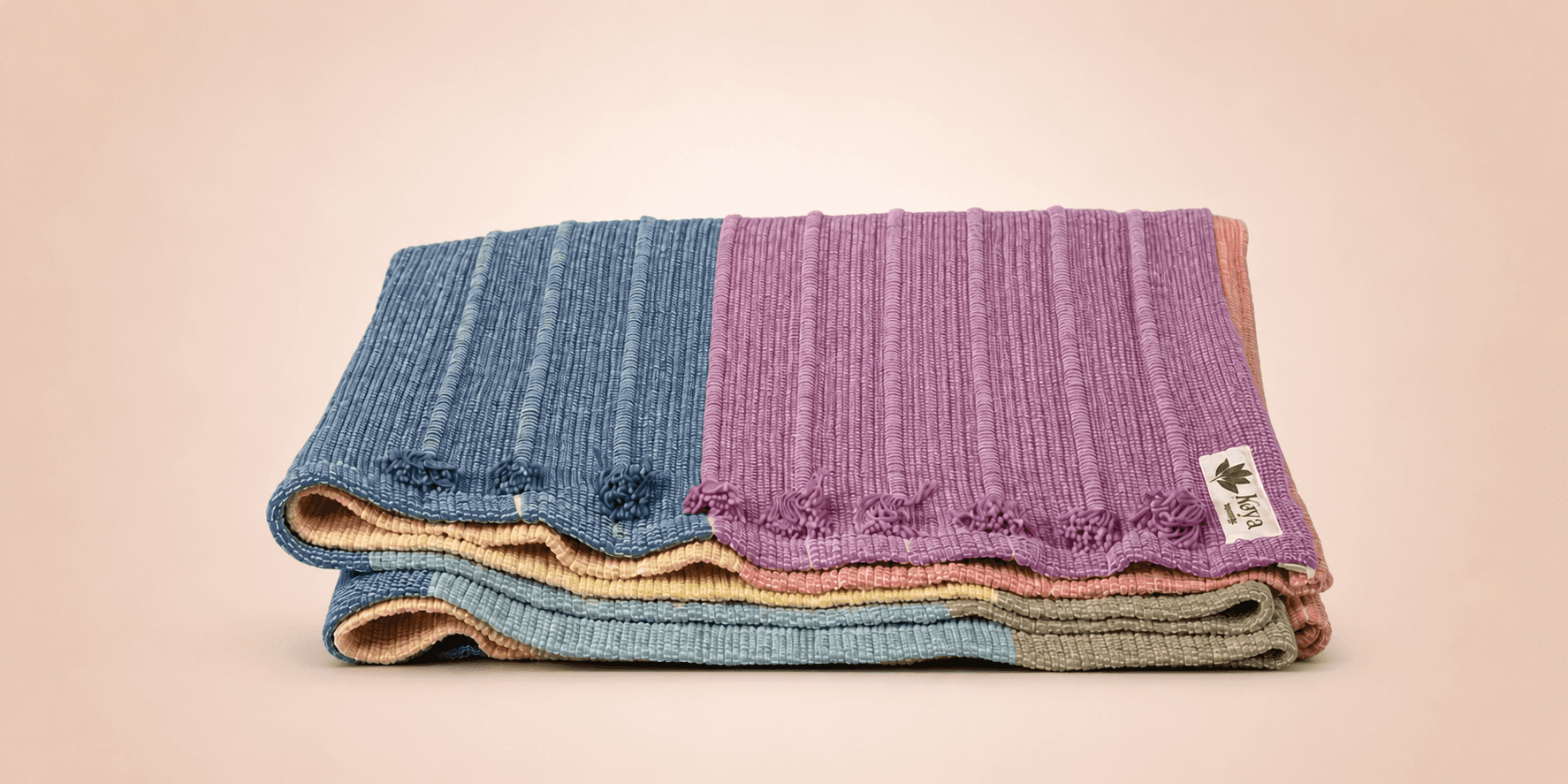 Folded organic cotton yoga rugs in pastel colors by Kaya Eco Living.
