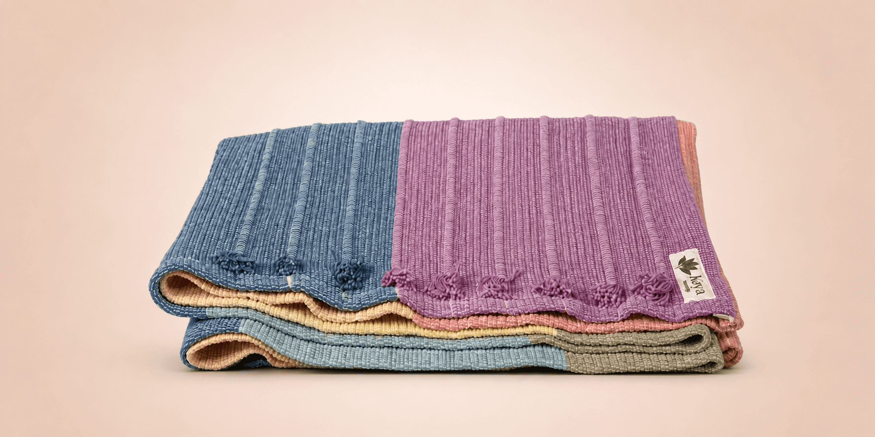 Folded organic cotton yoga rugs in pastel colors by Kaya Eco Living.