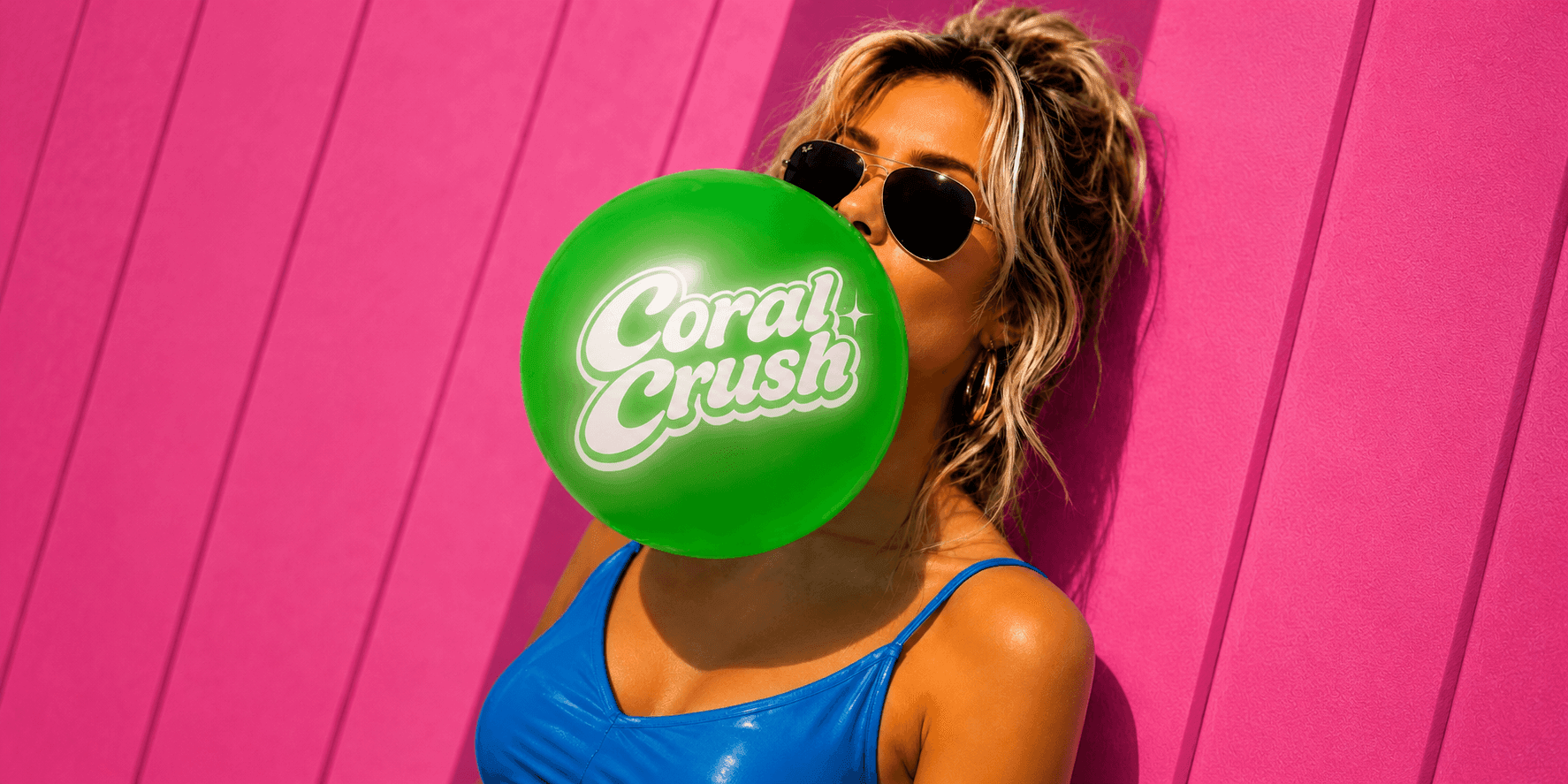 Person blowing a green Coral Crush balloon against a bright pink wall.