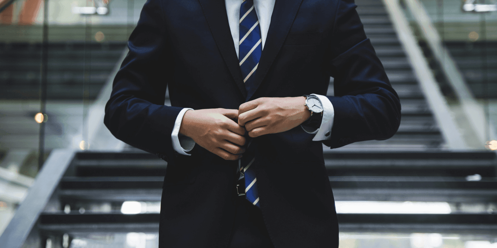 Business professional adjusting suit jacket on modern office staircase, symbolizing professionalism and corporate innovation.