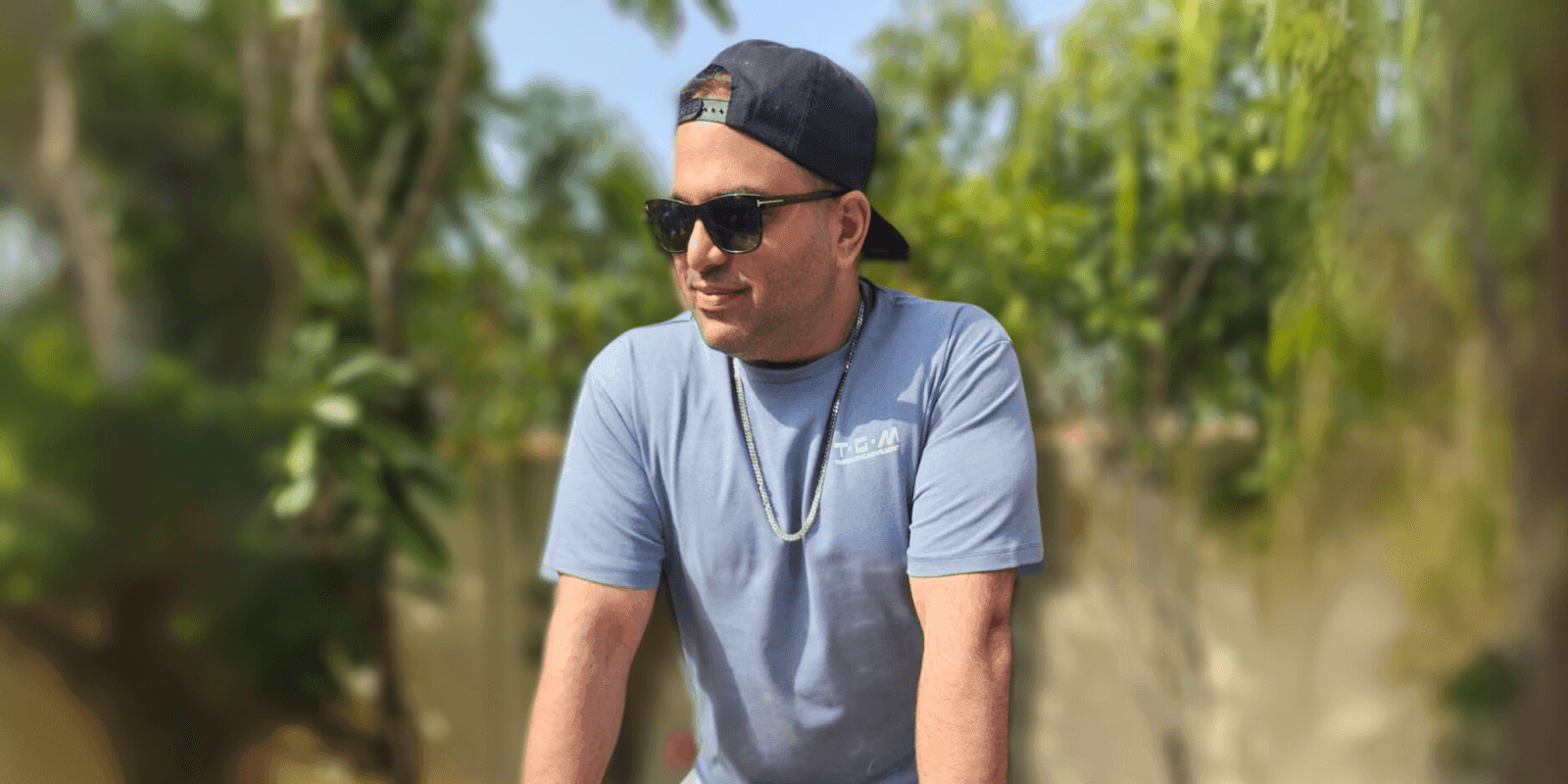 Aadil Datta wearing sunglasses and a cap, standing outdoors with greenery in the background.