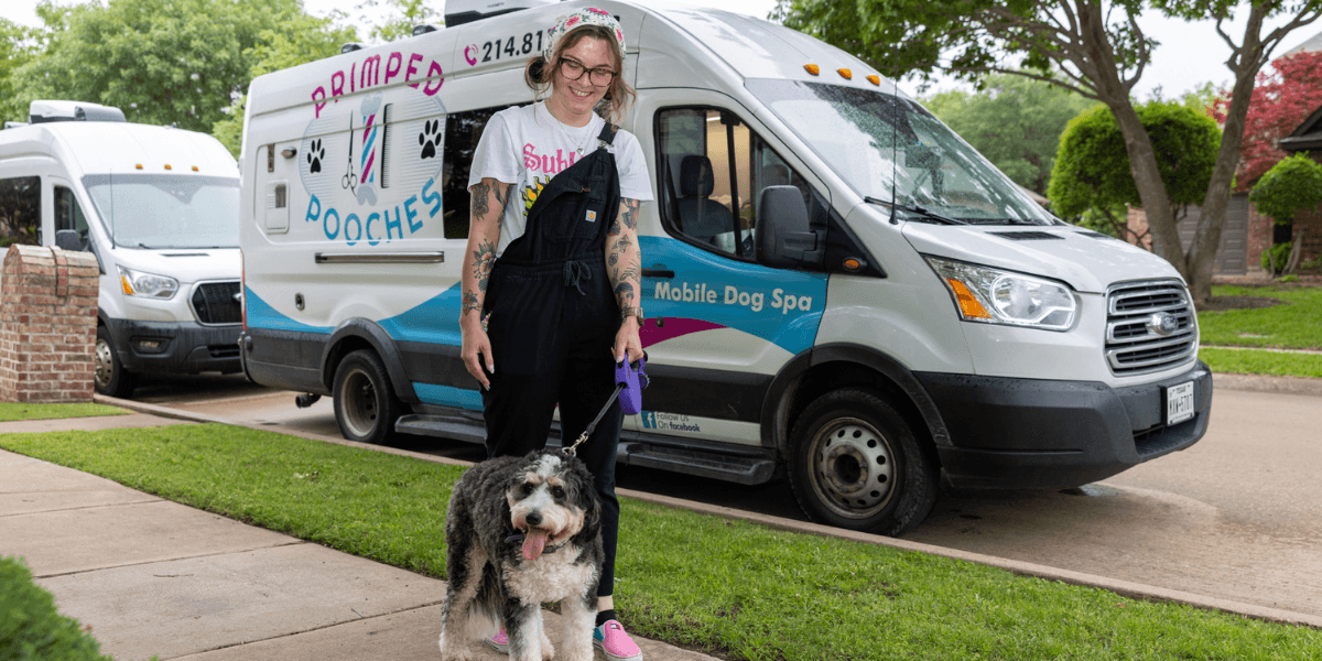 Owner of Primped Pooches stands with a dog outside her mobile dog spa van, offering personalized, stress-free grooming services.