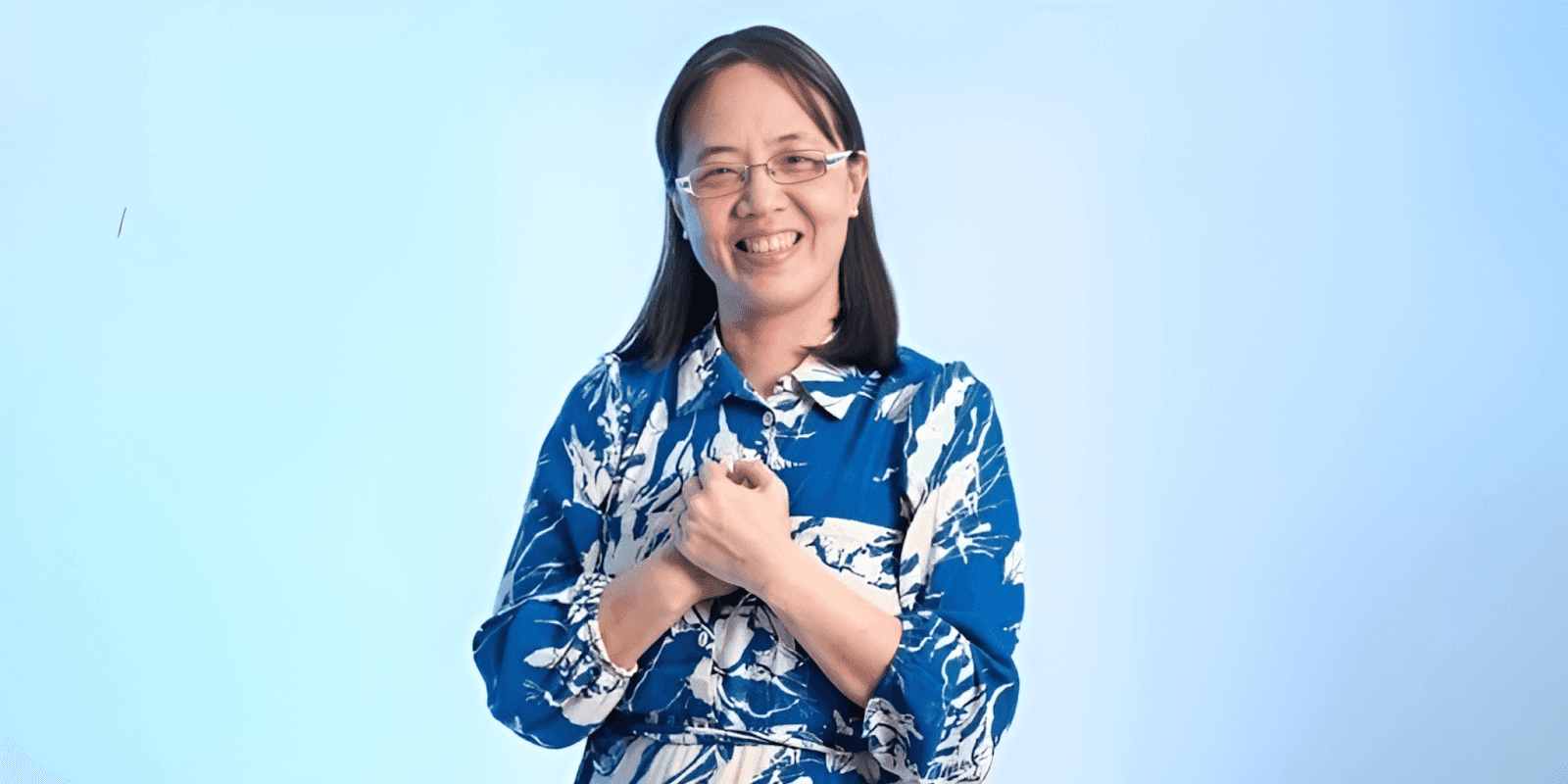 Smiling woman wearing a blue floral dress with a light blue background, expressing warmth and positivity.