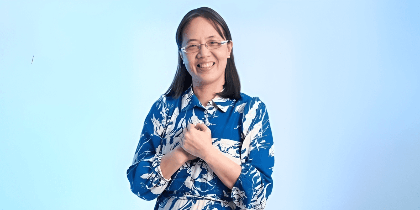 Smiling woman wearing a blue floral dress with a light blue background, expressing warmth and positivity.