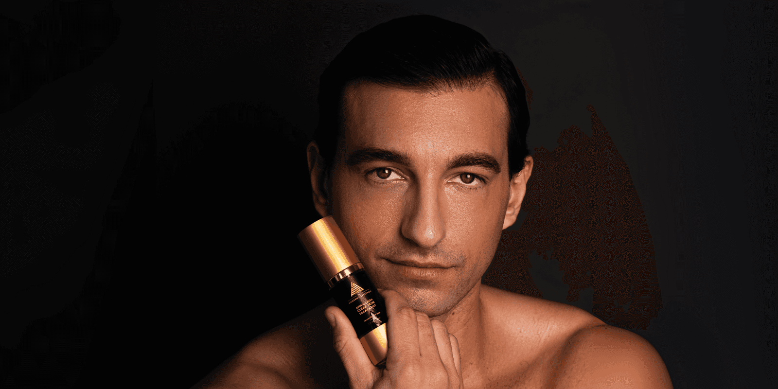 Man holding a luxury skincare product from The Modern Gentleman, highlighting a minimalist grooming routine with sleek black-and-gold packaging.
