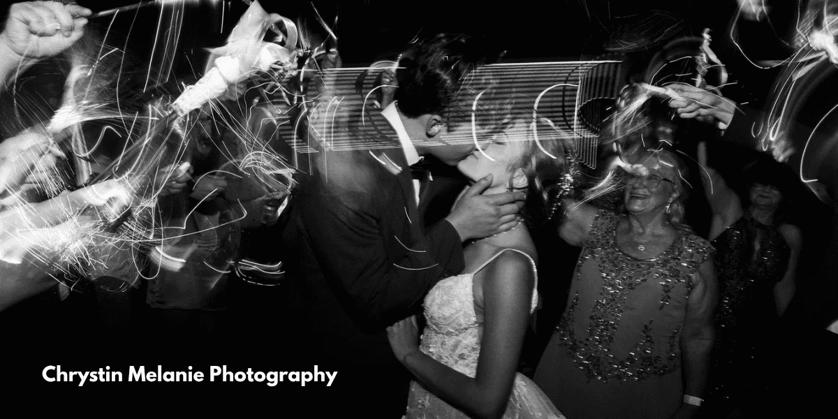 A bride and groom share a kiss, surrounded by glowing sparklers, capturing a magical moment of their wedding celebration.