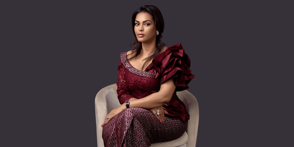Woman in elegant maroon dress seated confidently against dark background.