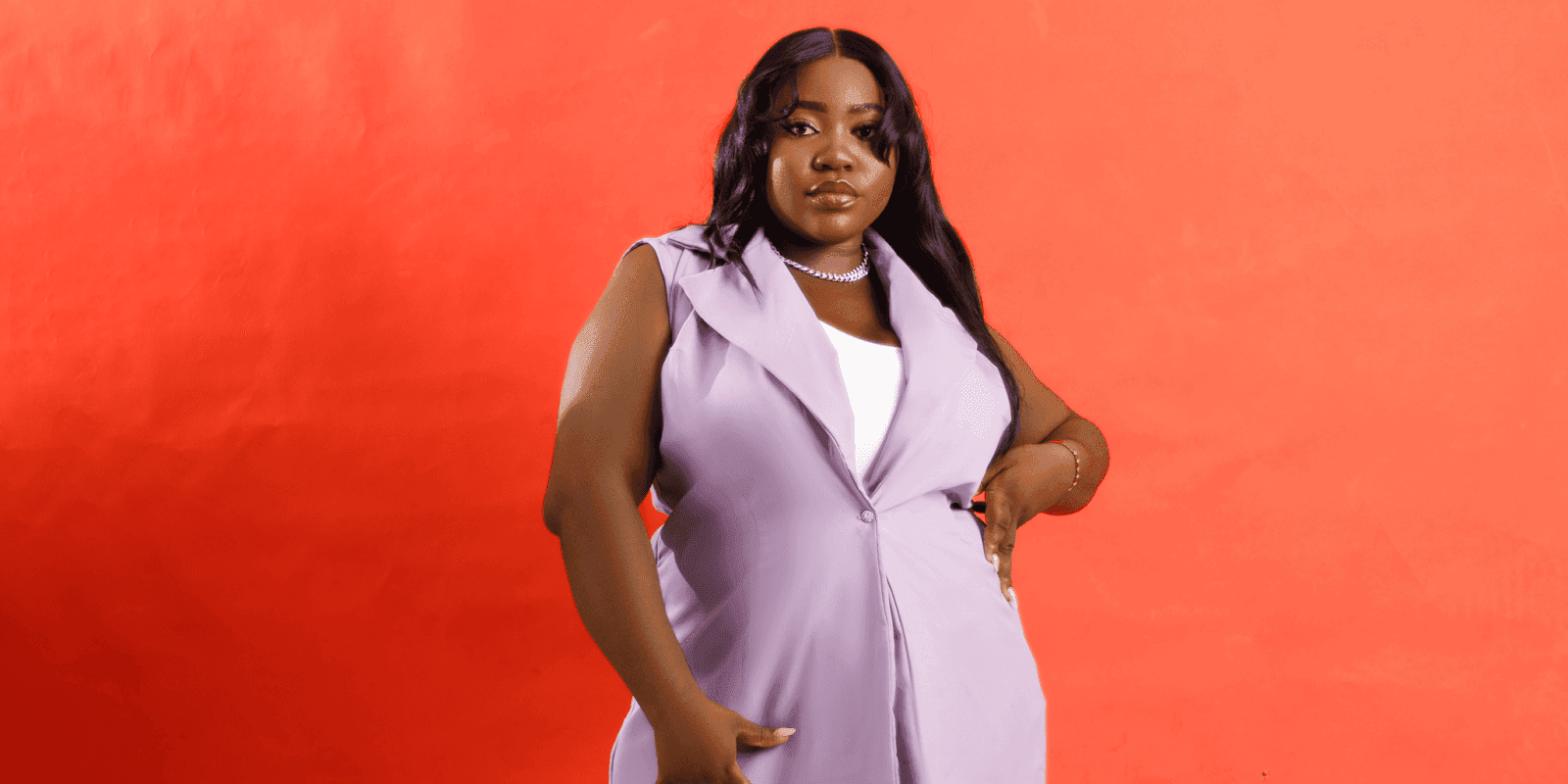 "A stylish woman dressed in a lavender blazer, standing against a vibrant red background, exuding elegance and confidence."