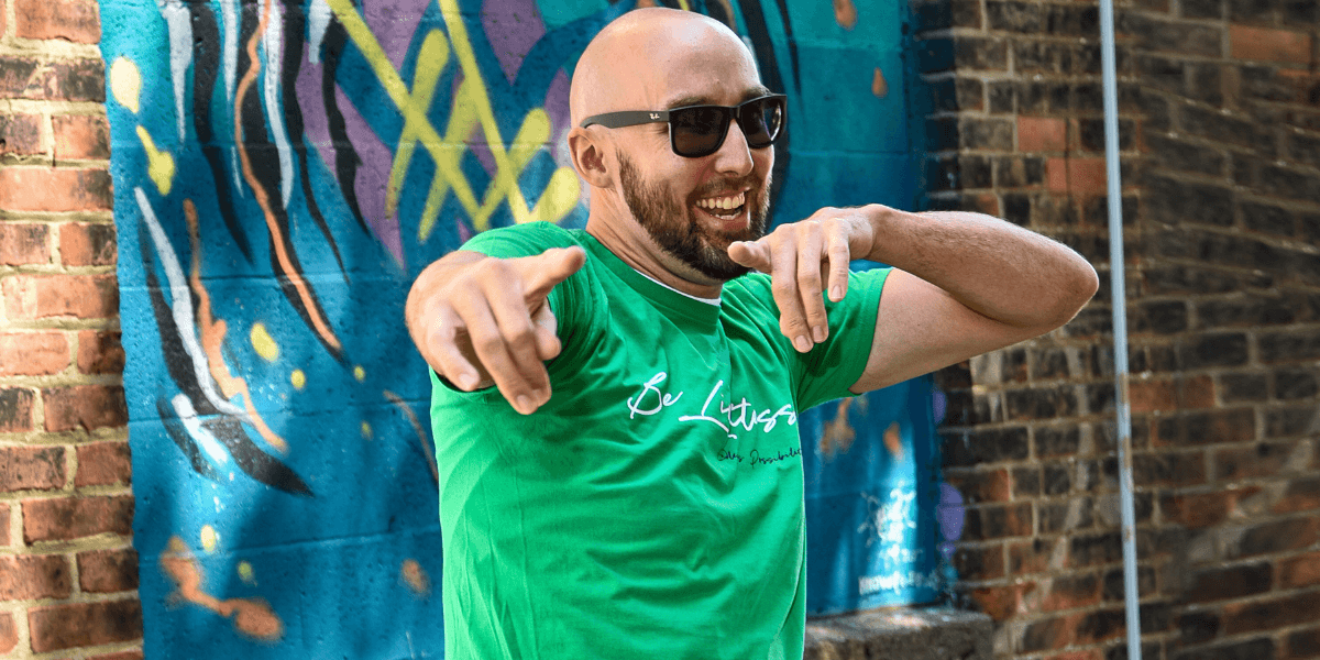 Joshua Williams smiling and pointing playfully, standing against a colorful graffiti wall, representing Limitless Innovation’s bold leadership approach.
