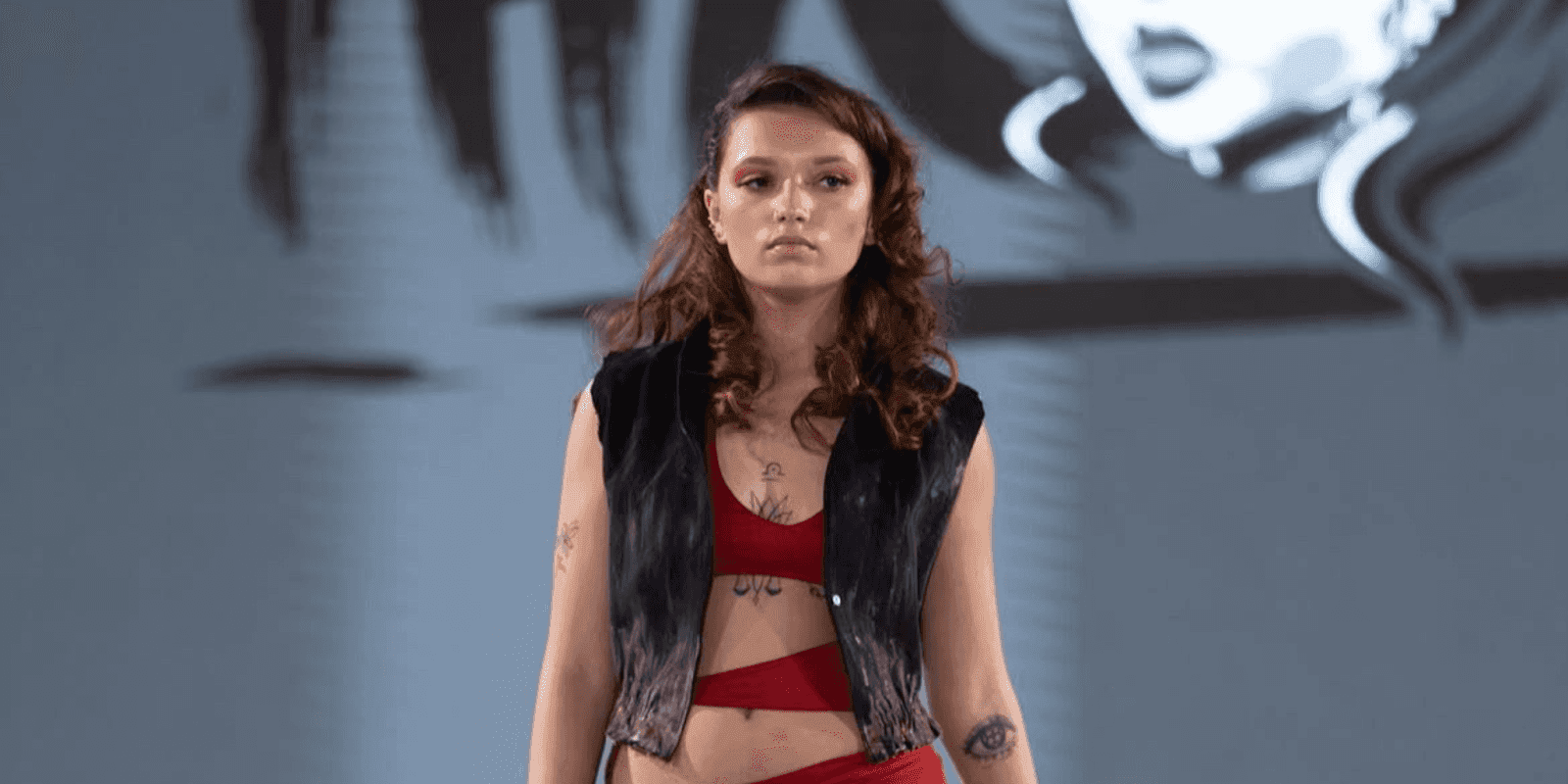 "Female model walking the runway at a fashion show, wearing a red outfit with a black vest, demonstrating a bold, trendy look."