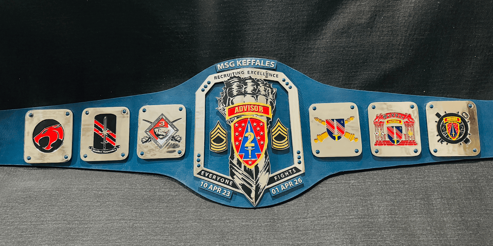 Military recruiting excellence championship belt with various unit insignias and the label 'ADVISOR' at the center, commemorating a period from April 2023 to April 2026