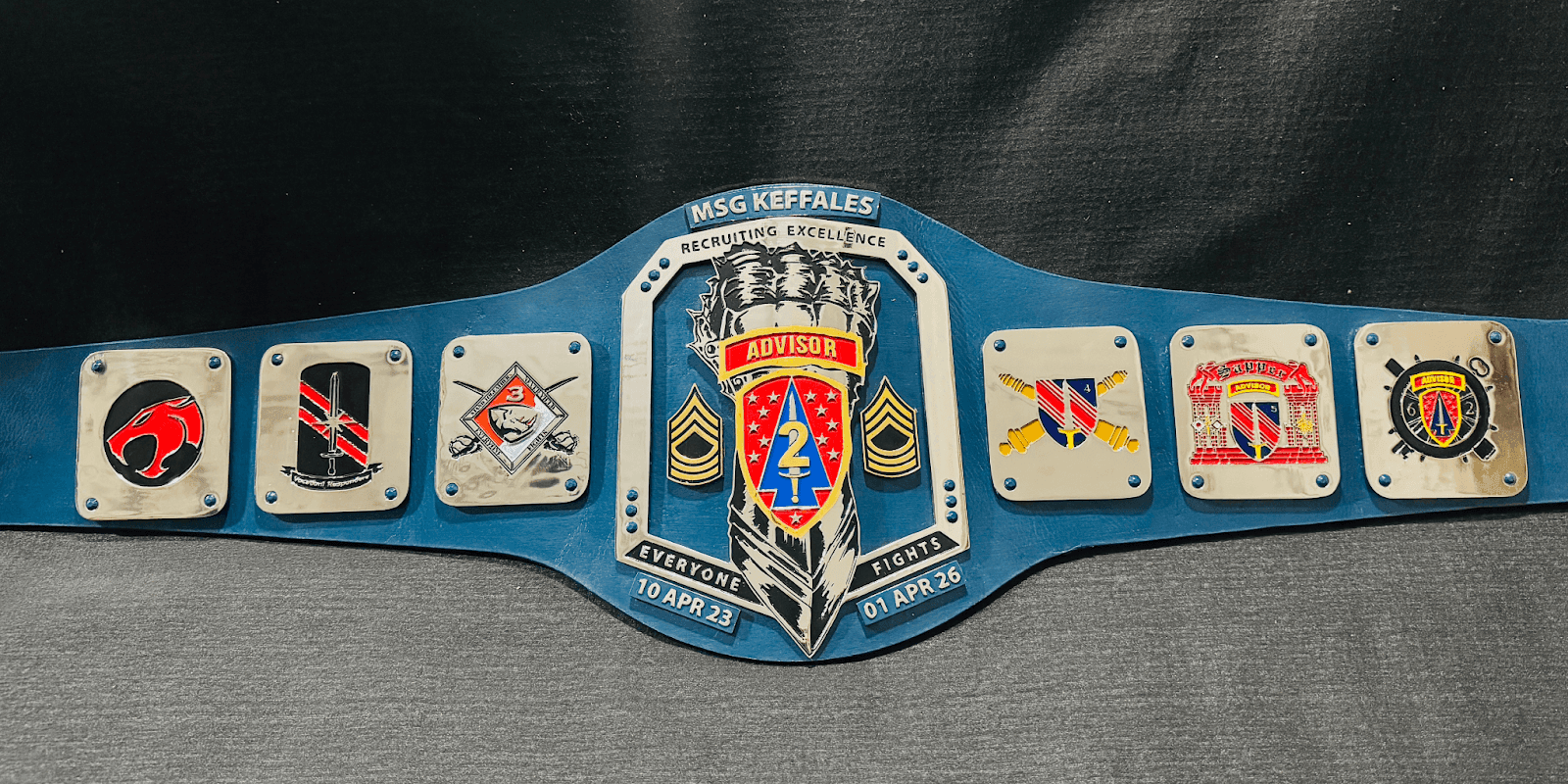 Military recruiting excellence championship belt with various unit insignias and the label 'ADVISOR' at the center, commemorating a period from April 2023 to April 2026