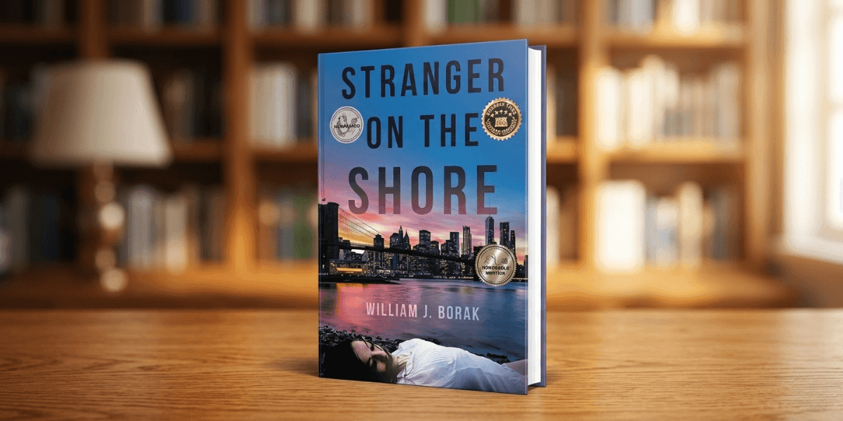 Book titled "Stranger on the Shore" by William J. Borak stands on a wooden table. The cover shows a city skyline at sunset with two award seals. A cozy library setting is blurred in the background.