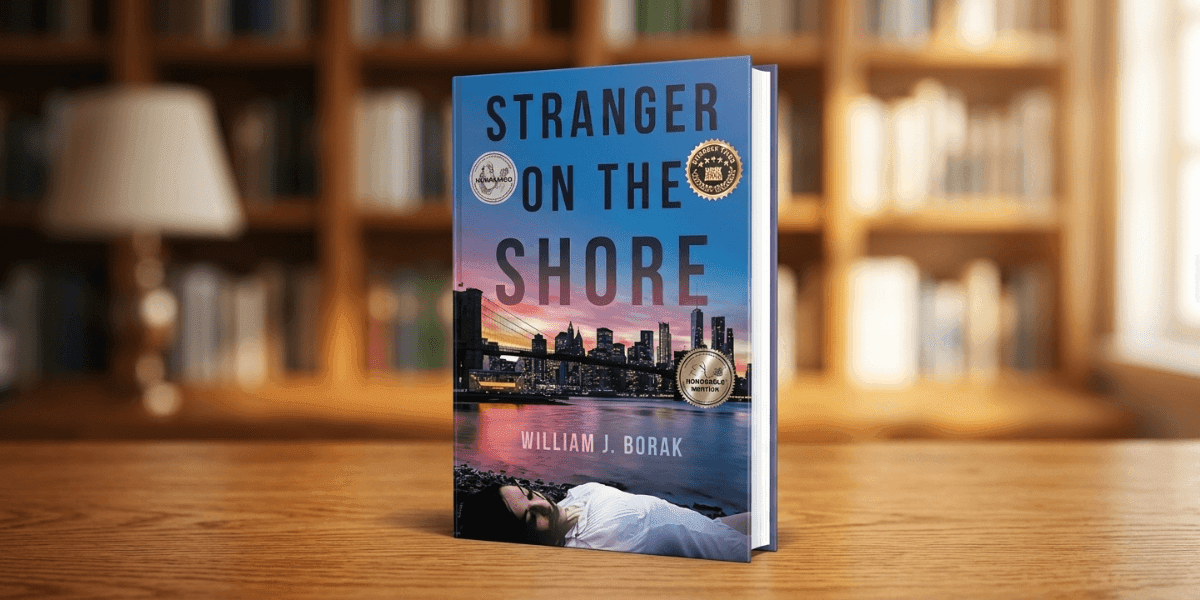 Book titled "Stranger on the Shore" by William J. Borak stands on a wooden table. The cover shows a city skyline at sunset with two award seals. A cozy library setting is blurred in the background.