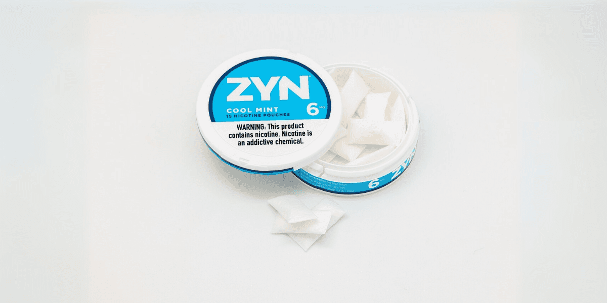 "Container of ZYN Cool Mint nicotine pouches with some pouches visible inside, labeled with a warning that the product contains nicotine, an addictive chemical."