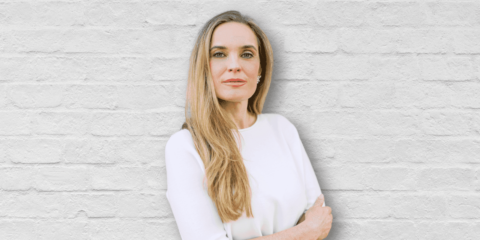 Woman in white outfit posing confidently against a light brick wall background.