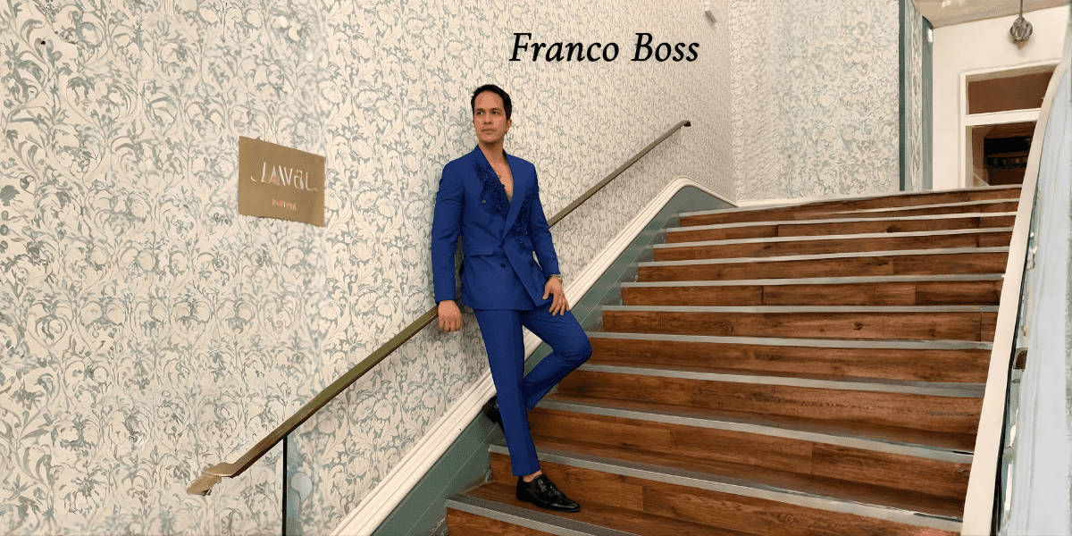 Fashion designer in blue suit posing on staircase beside Franco Boss branding.