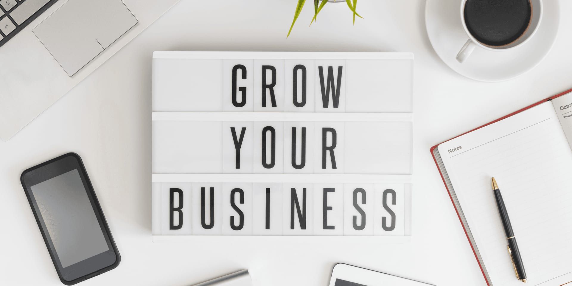 Desk with laptop, smartphone, coffee, notebook, and lightbox displaying “Grow Your Business.”