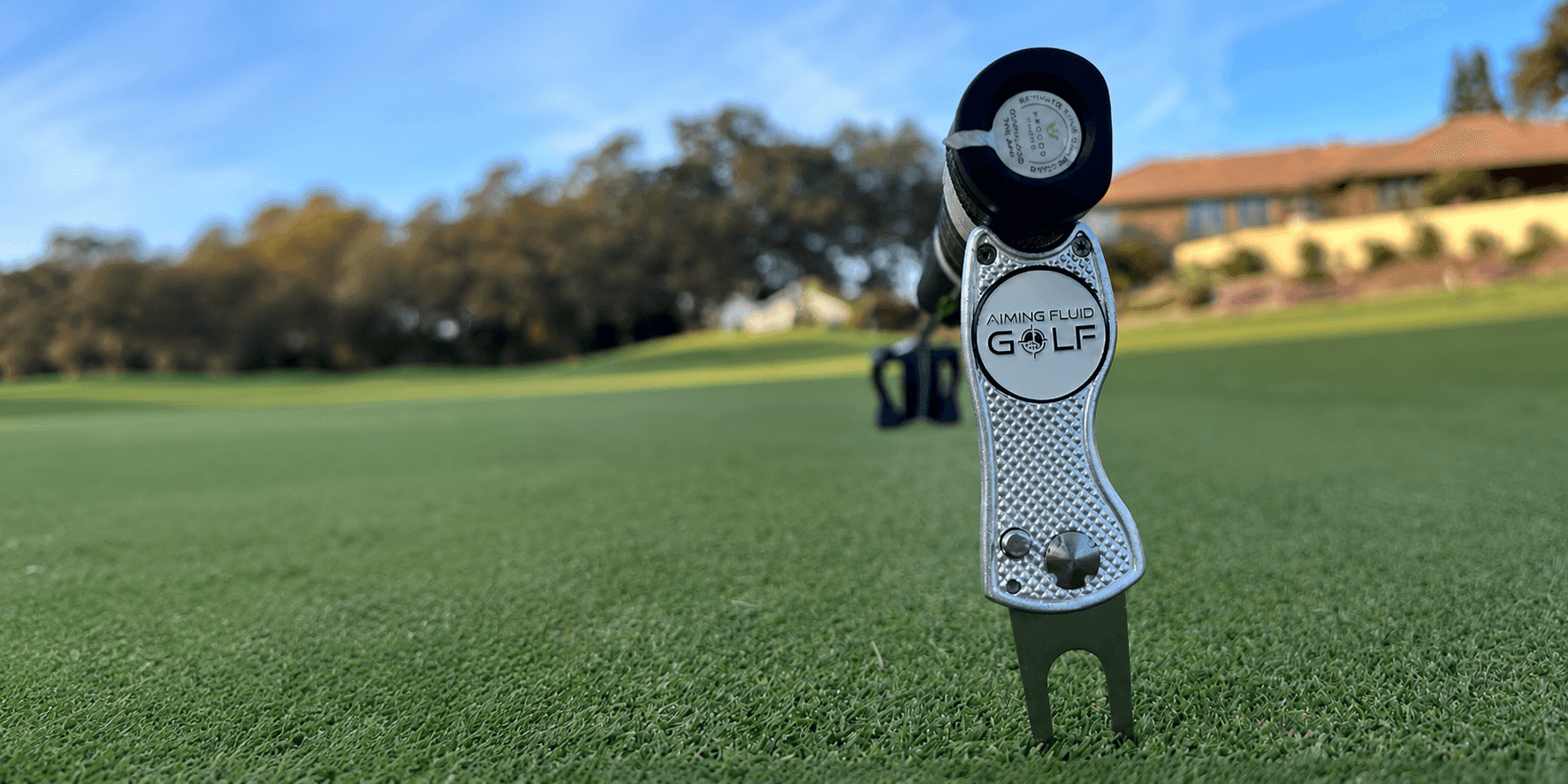 Aiming Fluid Golf divot repair tool standing upright on a green with course background.