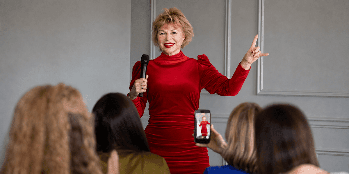 Dr. Agnieszka Piotrowska speaks into a microphone before an audience while wearing a red dress.