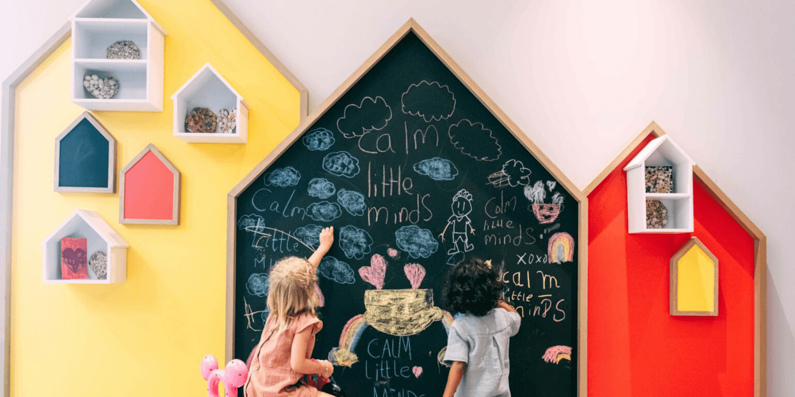 Children drawing on a colorful wall, engaging in emotional learning activities with a chalkboard that promotes calm minds.