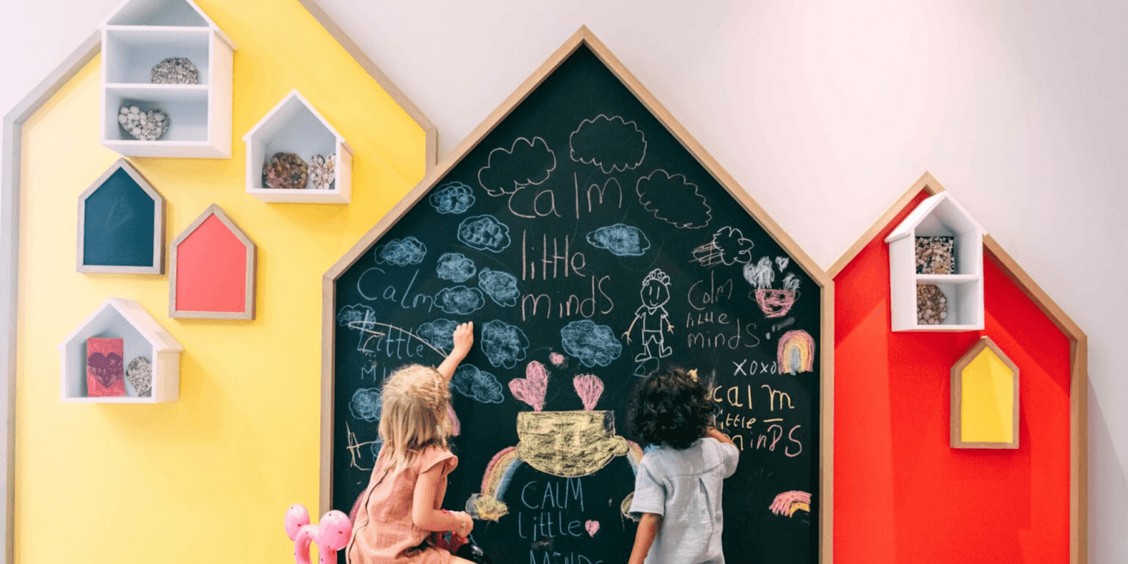 Children drawing on a colorful wall, engaging in emotional learning activities with a chalkboard that promotes calm minds.