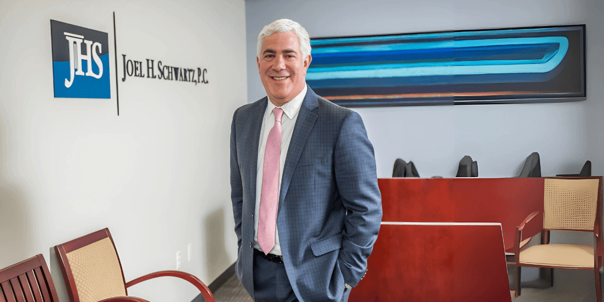 "Lawyer standing confidently in his office, dressed in a suit, in front of the Joel H. Schwartz, P.C. logo."