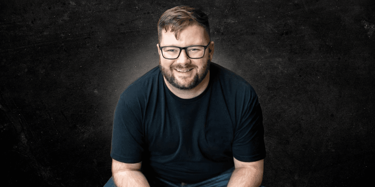 Will Craig smiling in glasses and a black shirt against a textured dark background.