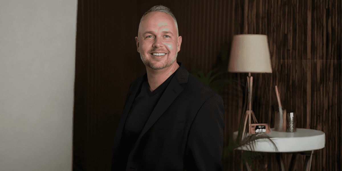 Mike Acker, an executive communication coach, smiling confidently in a black blazer against a stylish background.