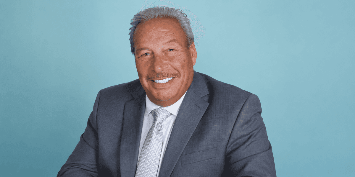 Ralph Black wearing a gray suit and tie against a light blue background.