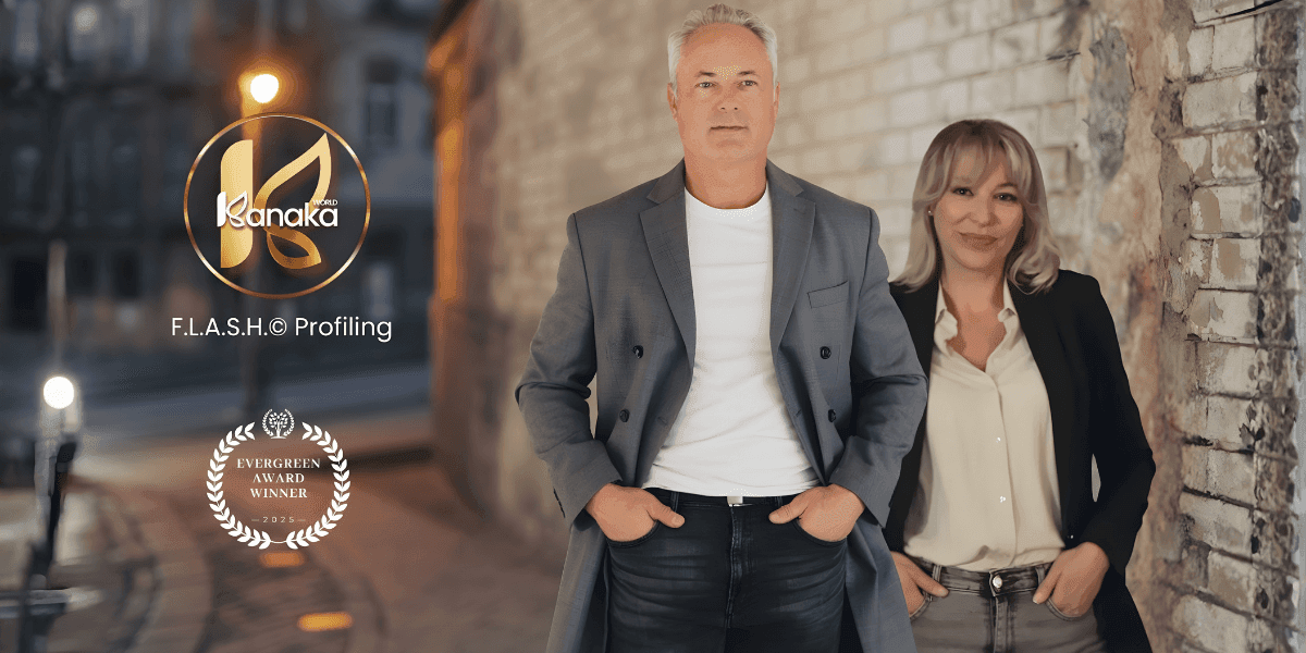 Man and woman leaning against a brick wall in a dimly lit street, both smiling. Logos for "Kanaka F.L.A.S.H.© Profiling" and "Evergreen Award Winner" are visible.