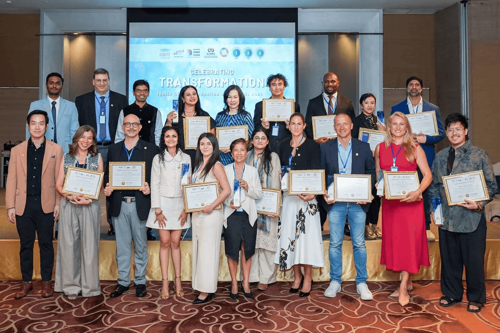 "Group photo of award recipients at the 'Celebrating Transformation' event hosted by Ignite Global Foundation. Individuals stand on stage holding certificates, representing diverse backgrounds and accomplishments in front of a digital backdrop with logos and event details."