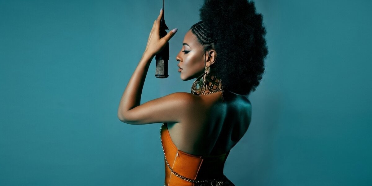 Debbi James holding microphone in profile against teal background during studio photoshoot.