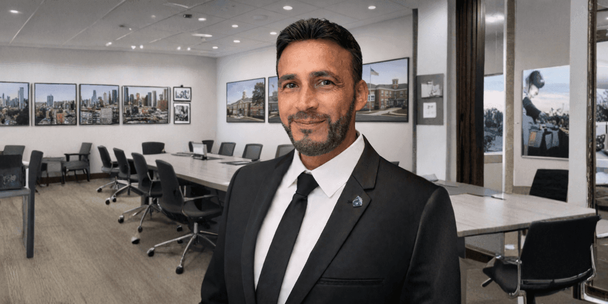 A professional man in a suit, standing in a modern conference room with large cityscape photos on the wall.