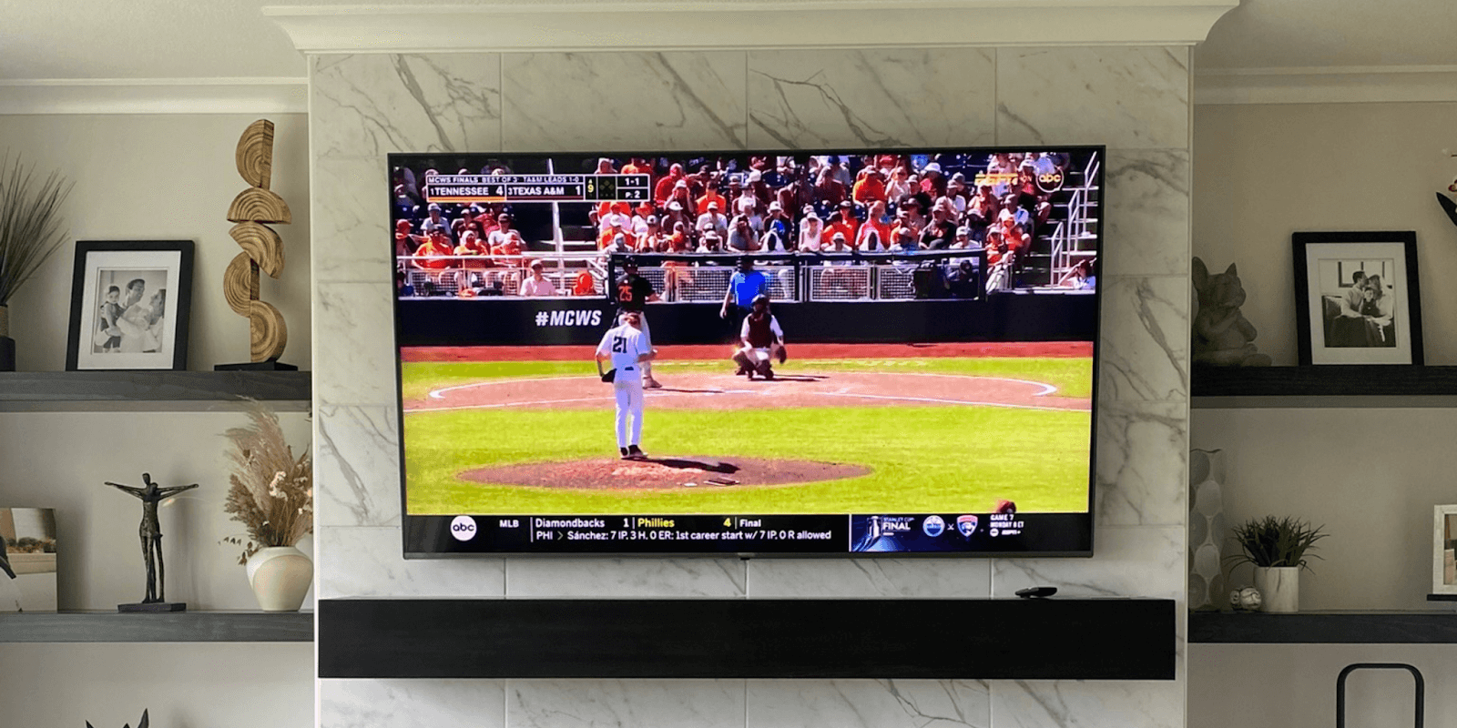 Mounted TV displaying a baseball game above a modern fireplace, showcasing SmartHome Connect’s expert installation work.