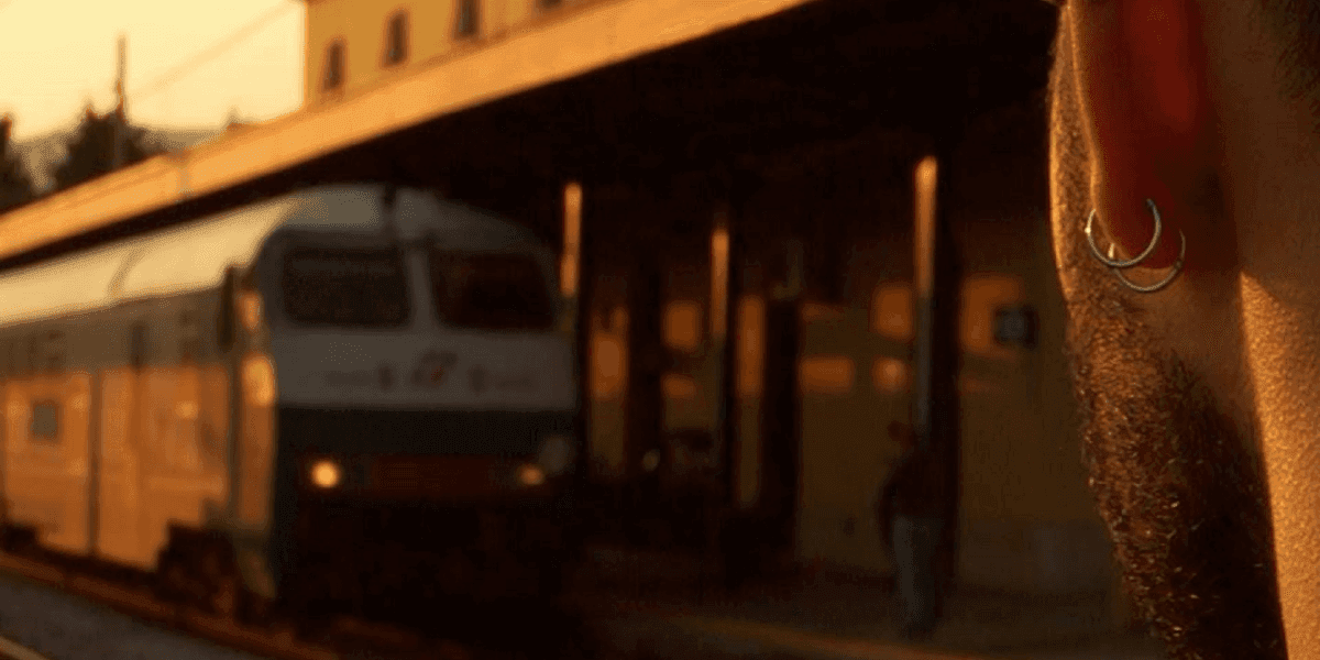 Man with earrings at sunset watching a train arrive at Battipaglia station, symbolizing Moicano Mc’s hip-hop journey.