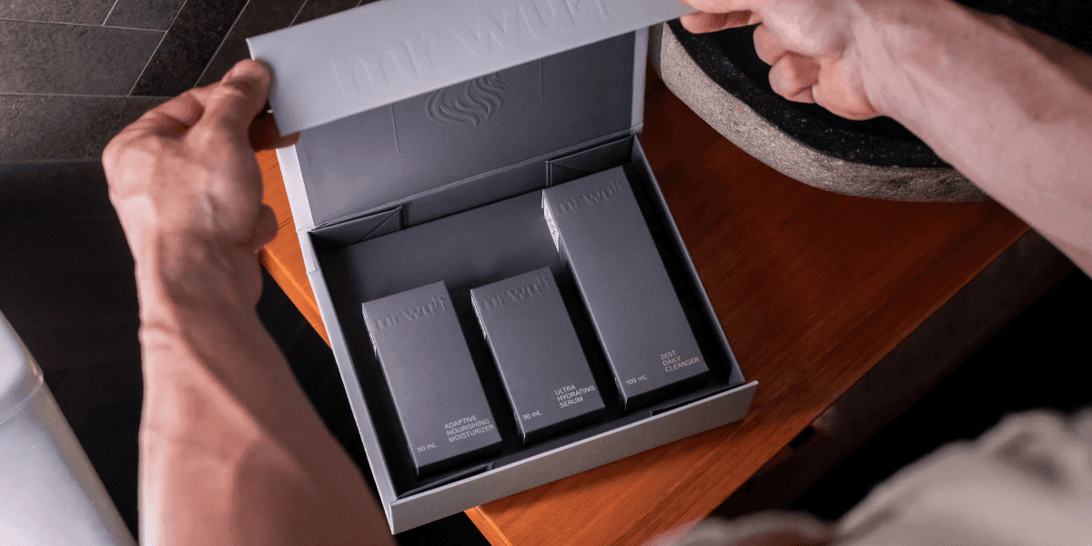 A person unboxing a skincare set from the brand 'mrwuf', showing the products inside the box: Adaptive Moisturizing Moisturizer, Ultra Hydrating Serum, and Zest Cleanser.