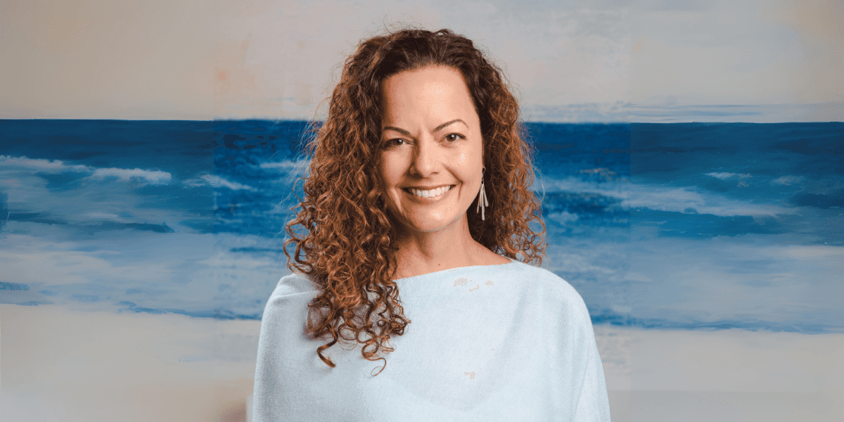 Julie Speetjens, Karuna Reiki Master, smiling before ocean backdrop, embodying transformation from corporate burnout to spiritual healing and empowerment.