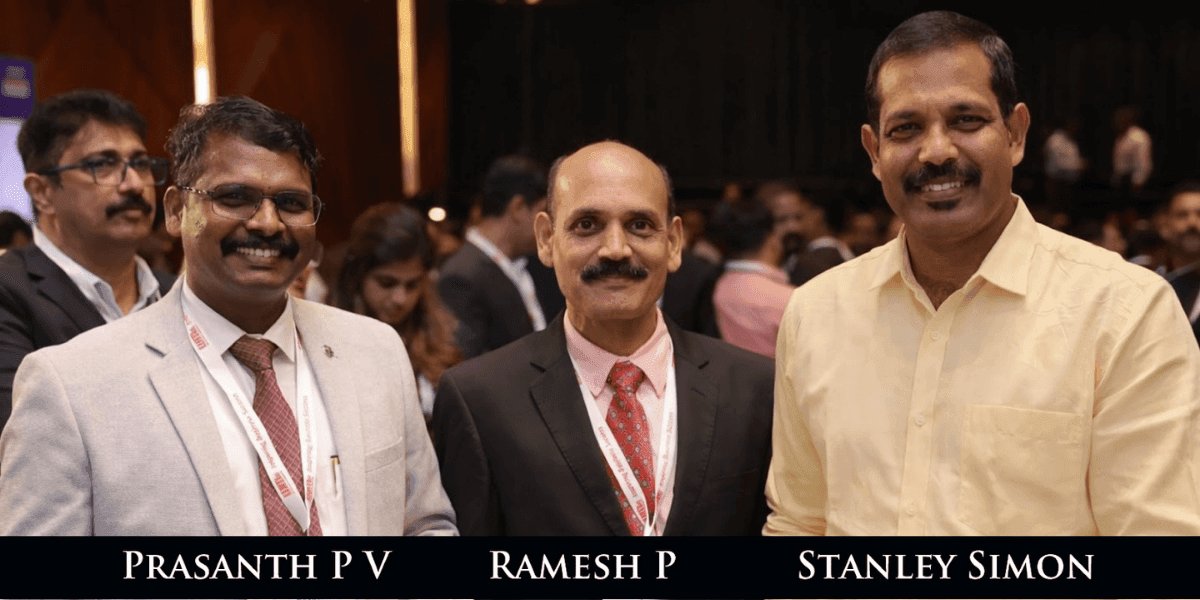 Three men in business attire stand smiling at an event. They are in a crowded room with blurred figures in the background, conveying a professional and friendly atmosphere.
